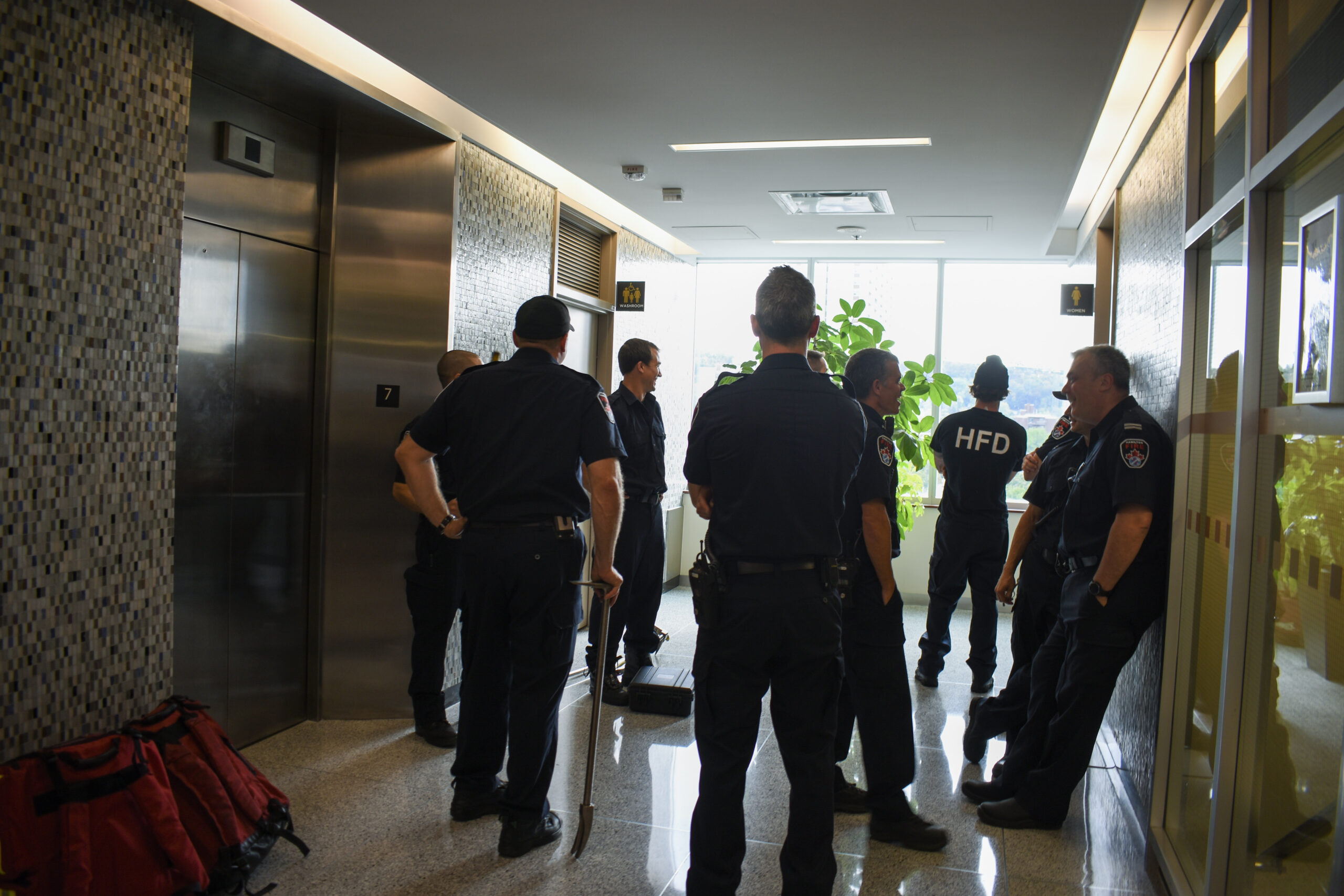 Hamilton firefighters standing in a lobby awaiting an elevator mechanic to rescue a person trapped inside a stalled elevator